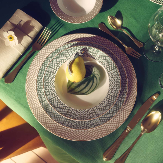 Stack of plates consisting of a place plate, dinner plate and deep plate on a table laid with a green tablecloth.